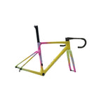 A bicycle frame with a vibrant yellow base and pink, green, and blue tie-dye accents, shown with black drop handlebars and black seat post on a light gray background.